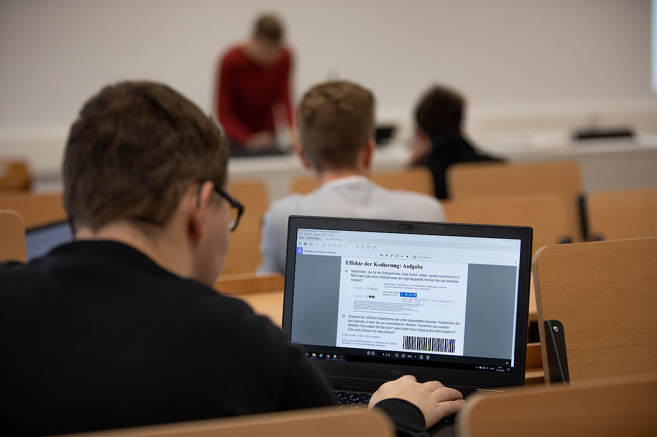 Symbolbild, Studierender sitzt im Hörsaal und verfolgt die Präsentation auf dem eigenen Laptop
