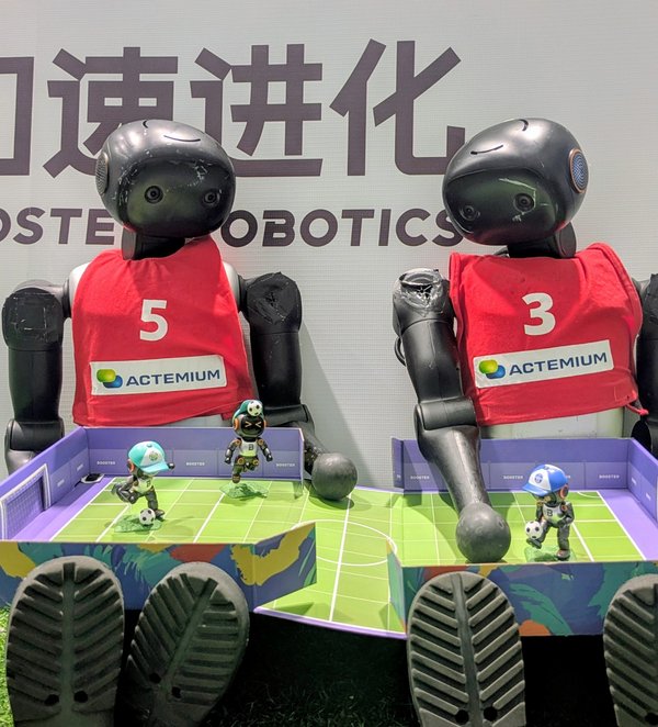 Lagebesprechung. (Foto: HTWK Robots) zwei humanoide Roboter sitzen nebeneinander vor einer Wand mit chinesischen Schriftzeichen