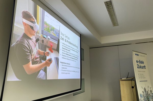 Leinwand zeigt Präsenatation mit Bild einer Person mit VR-Brille am Schreibtisch sitzend