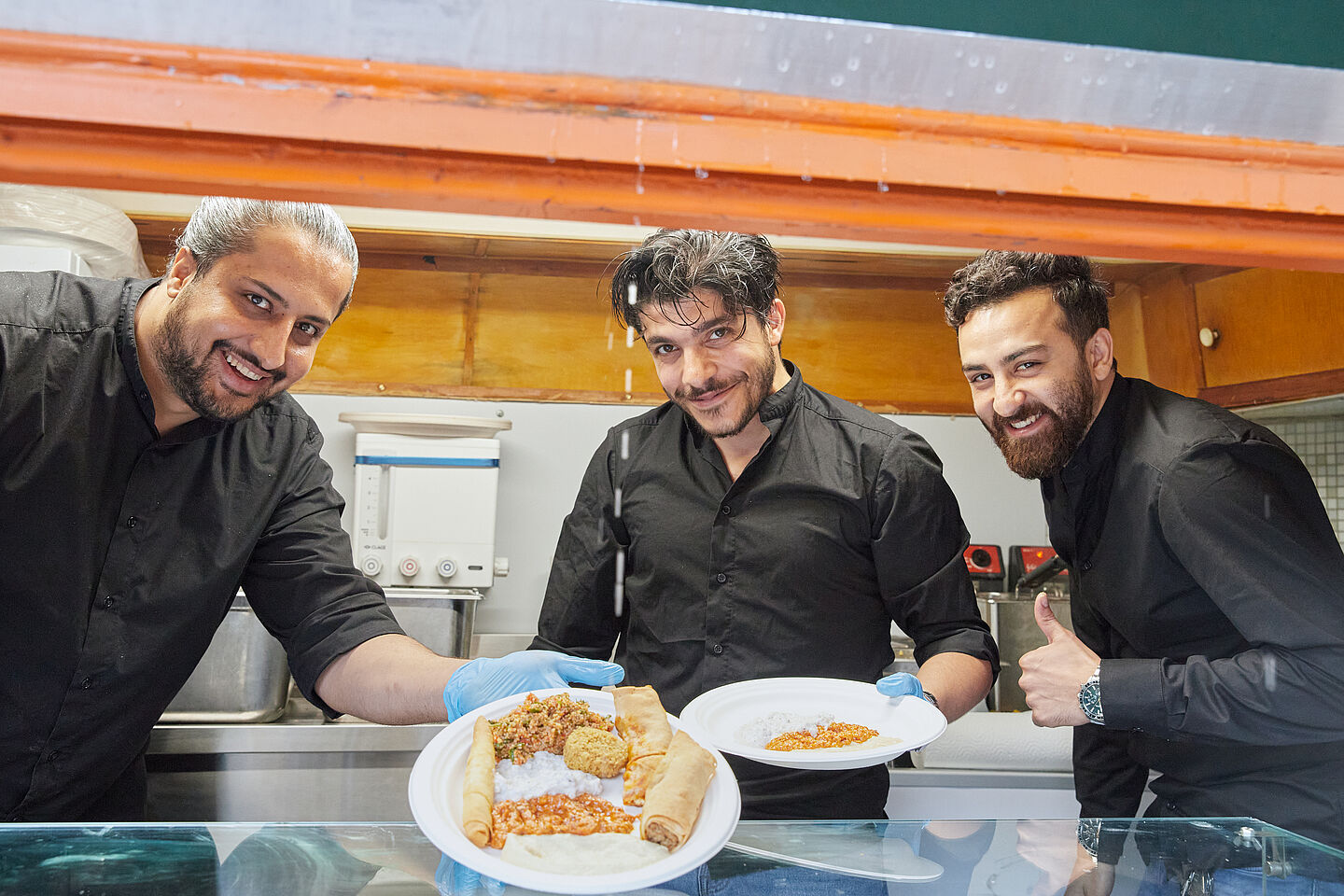 Drei Mitarbeiter von Maza Pita geben Essen aus