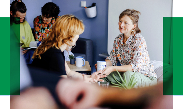 Fünf Personen sitzen in einem hellen Raum, unterhalten sich und trinken Kaffee. Zwei Frauen sprechen sich direkt gegenüber.. Zur Seite Unterstützung auf Augenhöhe mit Ment4Science.