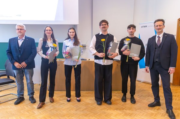 Gruppe von Studierenden mit Urkunden und zwei Professoren steht in einem Hörsaal