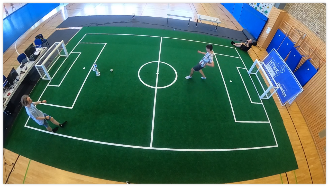 kleines Fußballfeld mit einem Roboter und zwei Menschen