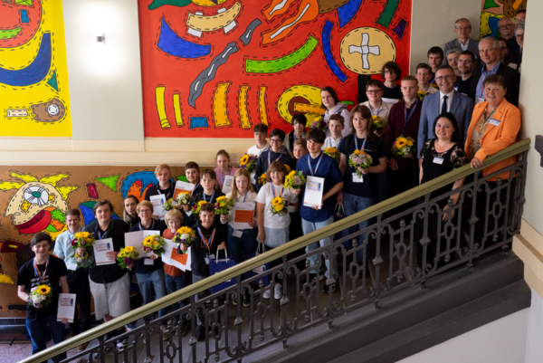 eine große Gruppe von Kindern und wenigen Erwachsenen steht auf einer Treppe in einem buntbemalten Treppenhaus